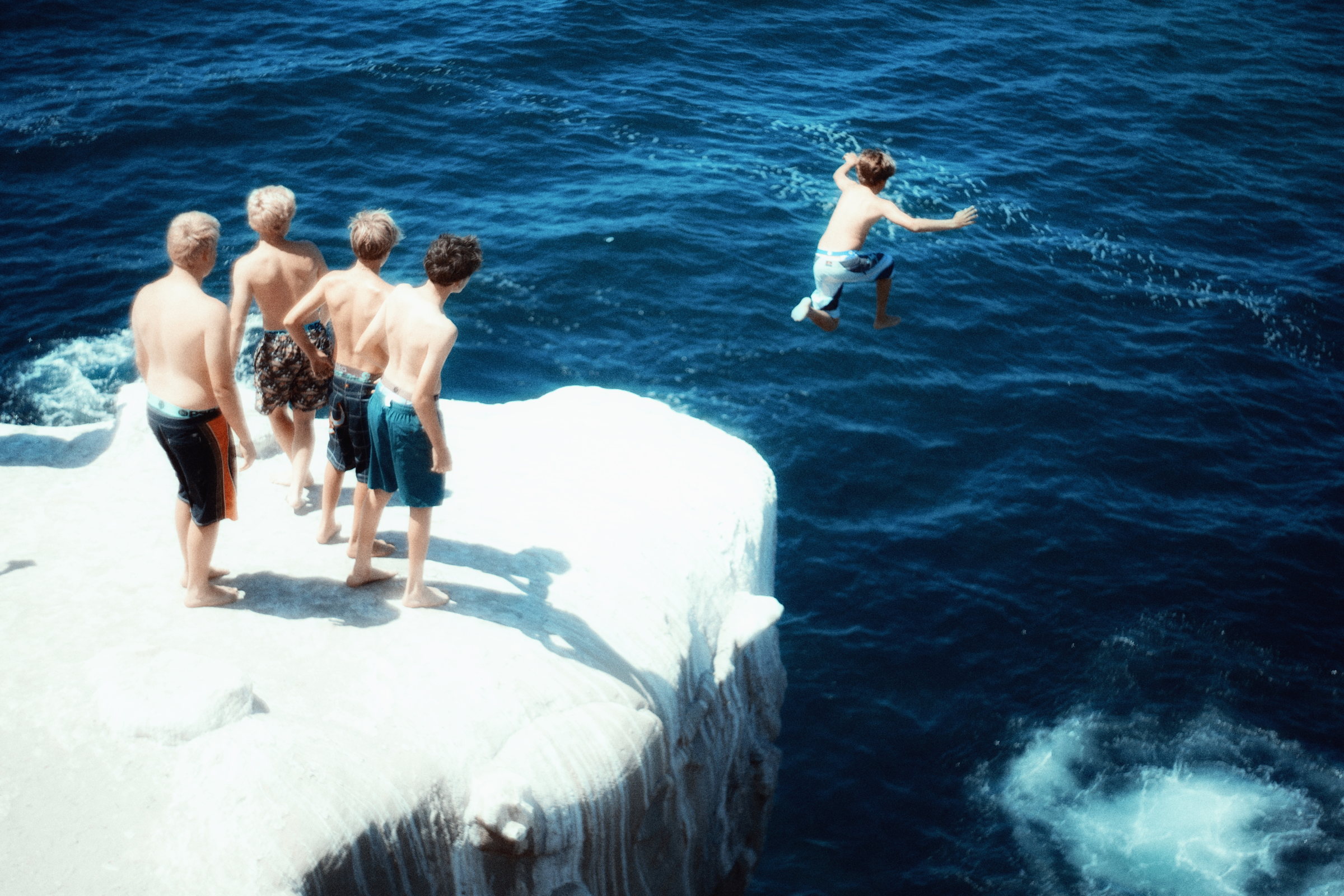 Swimmers jumping from a white seaside ledge